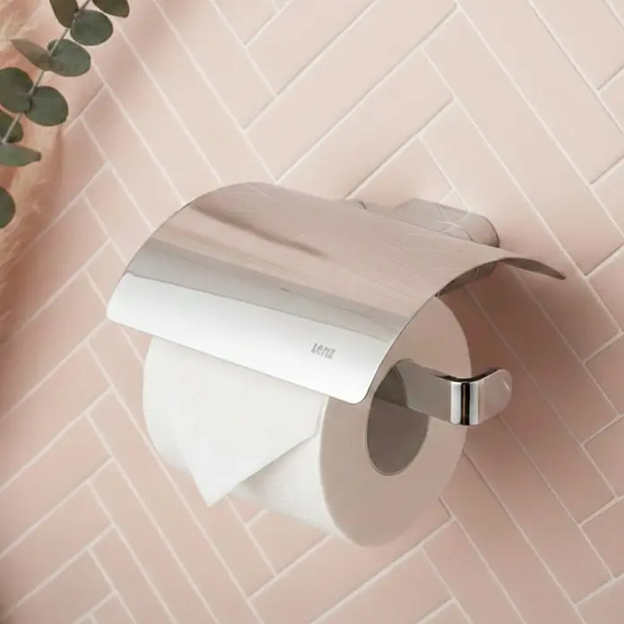 Lenz Aura Toilettenpapierhalter - Mit Deckel, Chrom, Glänzend - Verchromter Toilettenpapierhalter mit Abdeckung an einer rosafarbenen Fliesenwand, der eine Rolle Toilettenpapier hält.
