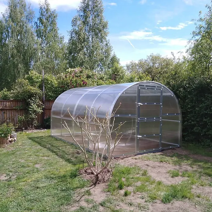 Klasika Greenhouses Gewächshaus Baltic Lt Klasika - Außenmaß inkl. Dachüberstand (B x T): 300 x 400 cm, Material Seitenwand: Kunststoff, 4 mm, Silbergrau - Klares, gewölbtes Polycarbonat-Gewächshaus in einem sonnigen Garten, bereit zur Bepflanzung.