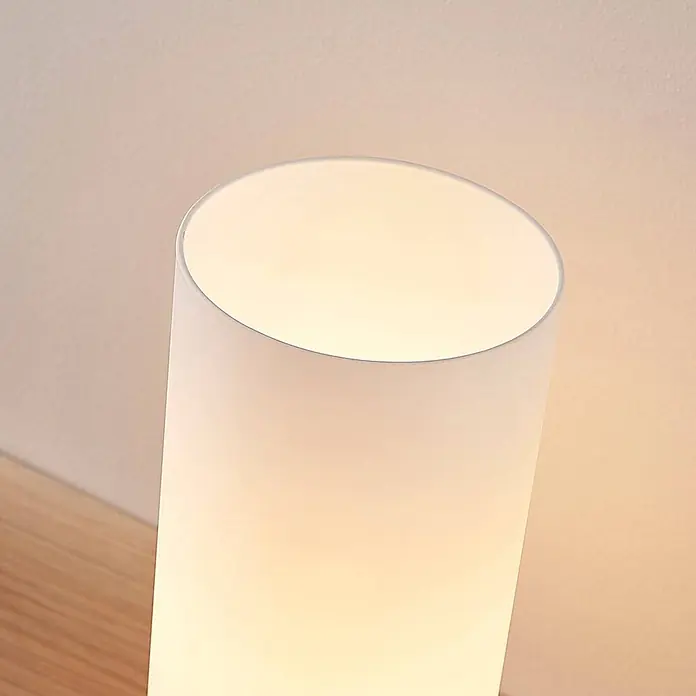 Lindby Tischleuchte Elianna - weiß / opal, E14 - Zylindrische weiße Lampe mit mattem Diffusor, die warmes Licht abstrahlt, auf einer Holzoberfläche.