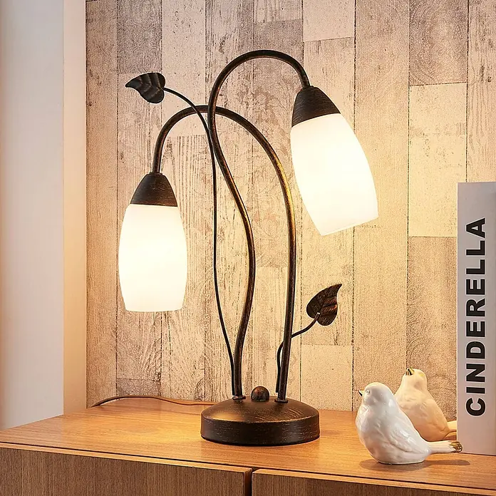 Lindby Tischleuchte Stefania - L x B x H: 28 x 28 x 40 cm, braun / rost, E14 - Bronze-farbene Tischlampe mit zwei weißen Glasschirmen und Zierblättern, die eine Holzoberfläche beleuchtet.