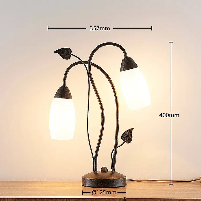 Lindby Tischleuchte Stefania - L x B x H: 28 x 28 x 40 cm, braun / rost, E14 - Bronzefarbene Tischleuchte mit zwei Lichtern, dekorativen Blättern und weißen Glasschirmen auf einem Holztisch.