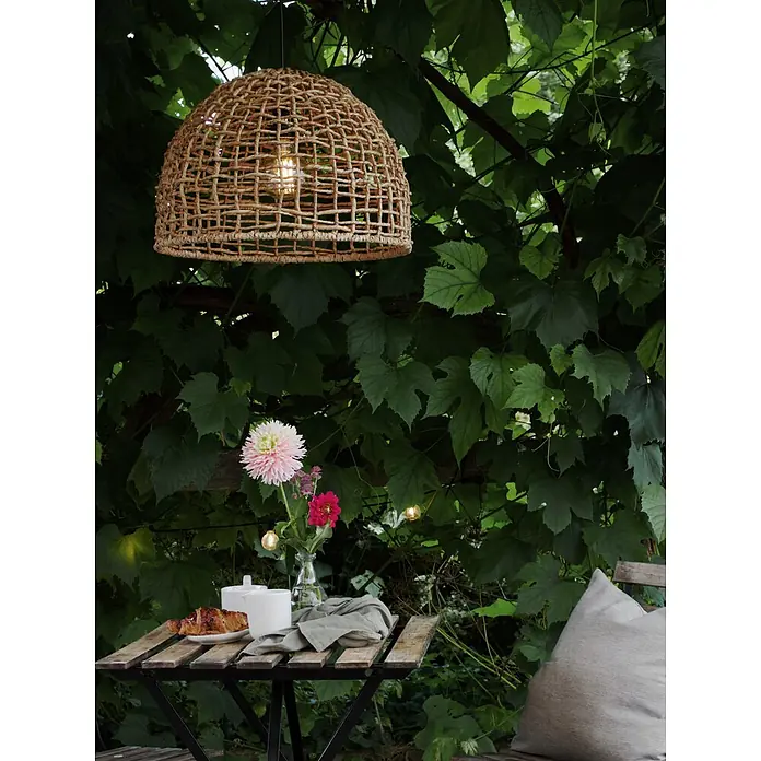 PR Home Pendelleuchte 46cm Outdoor - 40 W, E27 - Natürliche, geflochtene Hängelampe aus Weide hängt draußen über einem Frühstückstisch mit Blumen und spendet warmes Licht.