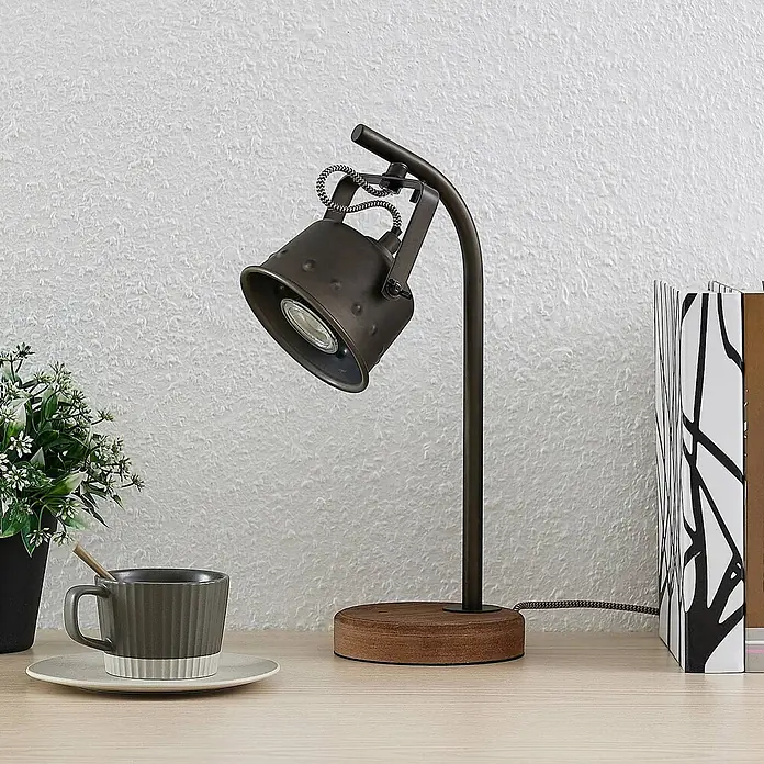 Lindby Tischleuchte Rubinjo - L x B x H: 20 x 13 x 36,5 cm, Holz dunkel, schwarz, GU10 - Dunkle Metall-Tischleuchte mit verstellbarem Strahlerkopf und Holzfuß auf hellem Schreibtisch, umgeben von Pflanze, Tasse und Büchern.