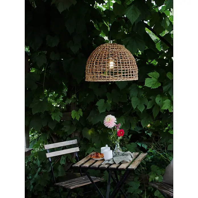 PR Home Pendelleuchte 46cm Outdoor - 40 W, E27 - Natürliche geflochtene Pendelleuchte beleuchtet ein Outdoor-Frühstück mit Tisch und Stühlen inmitten üppigen Grüns.