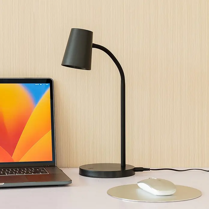 Lindby Tischleuchte Ailina - schwarz, schwarz - Schwarze Schreibtischlampe mit gebogenem Arm auf einem Tisch, neben Laptop und Maus.