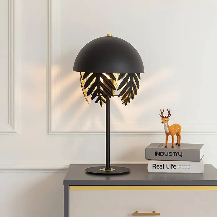 Lucande Tischleuchte Aparas - L x B x H: 28 x 28 x 54 cm, schwarz, schwarz, E27 - Schwarze Metall-Tischlampe mit Kuppelschirm und filigranen Goldblatt-Ausschnitten auf einem Nachttisch.