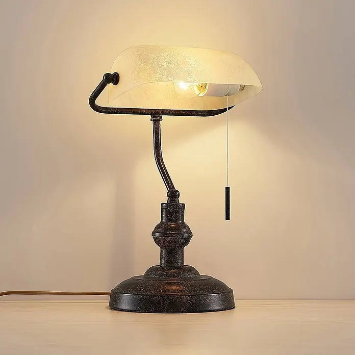 Lindby Tischleuchte Profina - L x B x H: 18,5 x 27,2 x 38,5 cm, braun / rost, creme / amber, E27 - Eine Bankerlampe mit antik bronzefarbenem Metallsockel, geschwungenem Arm und mattiertem Marmorglasschirm, beleuchtet.
