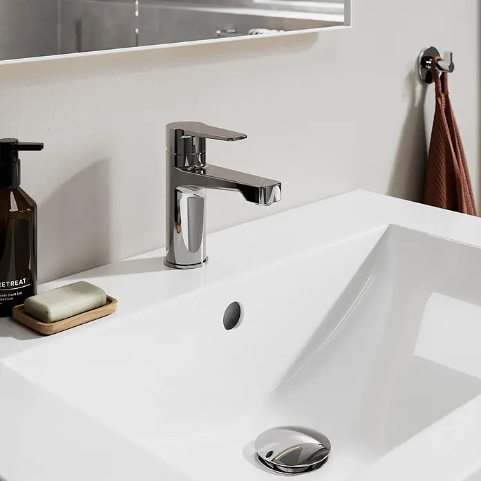Lenz Mola Waschtischarmatur - Chrom, Glänzend - Ein eleganter Chrom-Wasserhahn auf einem weißen Keramikwaschbecken im Bad, mit Seifenspender und Naturseife auf einer Holzschale.
