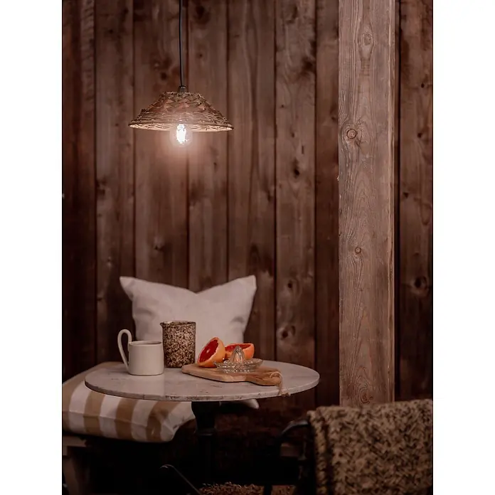 PR Home Pendelleuchte 27cm Outdoor - 40 W, E27 - Eine geflochtene Hängelampe beleuchtet eine gemütliche Ecke mit kleinem Tisch und Erfrischungen, was eine warme Atmosphäre schafft.