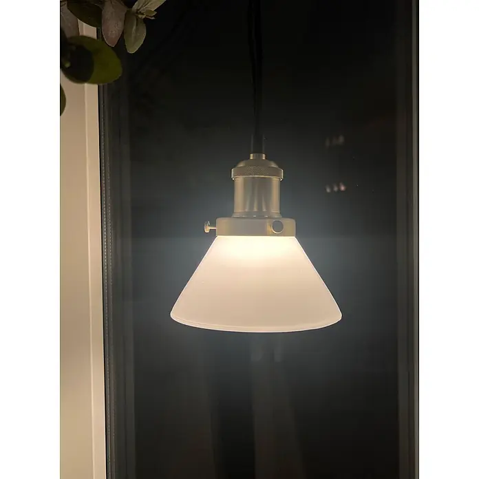 PR Home Pendelleuchte Fensterleuchte - 25 W, E27 - Beleuchtete Messing-Pendelleuchte mit mattweißem konischem Schirm, vor einem Fenster hängend.