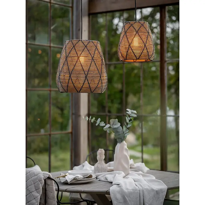 PR Home Pendelleuchte 38cm Outdoor - 40 W, E27 - Zwei geflochtene Rattan-Pendelleuchten mit dunklen Akzenten, beleuchtet über einem gedeckten Esstisch in einem Gewächshaus hängend.