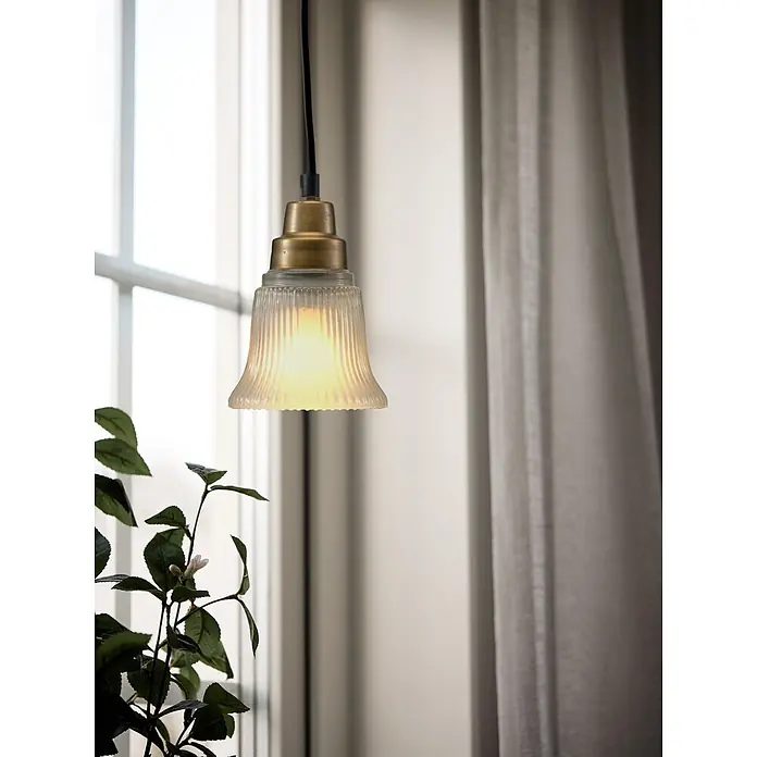 PR Home Pendelleuchte Emmi - 25 W, E27 - Eine messingfarbene Pendelleuchte mit geripptem Glasschirm hängt und wirft ein warmes Licht in einen Raum mit Fenster.