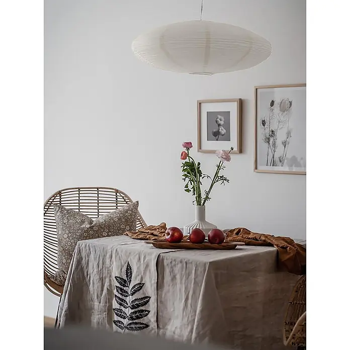 PR Home Pendelleuchte Lampenschirm -  - Esstisch mit einer natürlichen Leinentischdecke mit dunklem Blattmuster, daneben ein geschwungener Rattanstuhl.