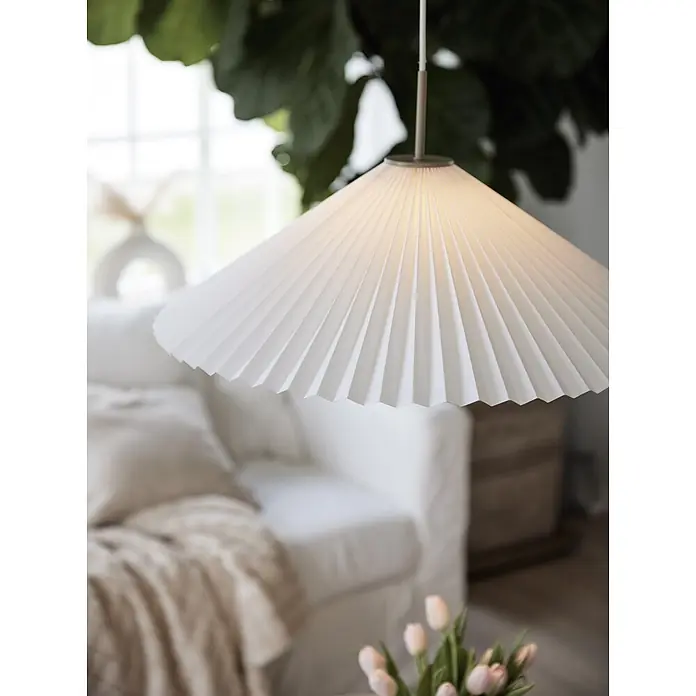 PR Home Pendelleuchte Dora - 25 W, E27 - Weiße plissierte Papier-Pendelleuchte mit warmem Licht, hängt in einem gemütlichen Wohnzimmer.