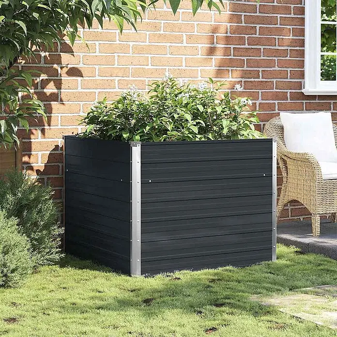 Furnicato Hochbeet - 100 x 100 x 77 cm, Stahl, Anthrazit - Dunkelgrauer Lamellen-Pflanzkasten mit silbernen Ecken, gefüllt mit Grünpflanzen und weißen Blüten, im Gras im Freien.