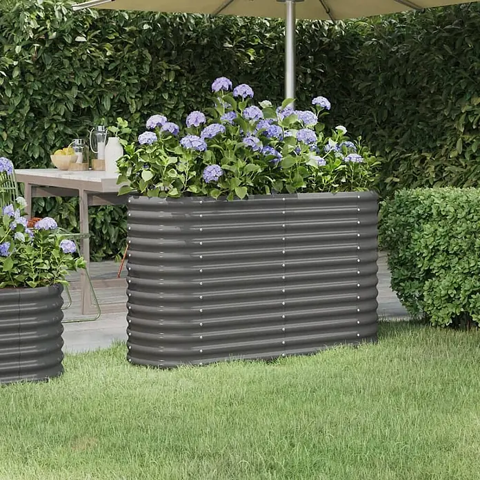 Furnicato Hochbeet - 114 x 40 x 68 cm, Stahl, Grau - Großes dunkelgraues Hochbeet aus Wellblech mit lila Blumen im Garten, daneben ein kleinerer passender Pflanzkübel.