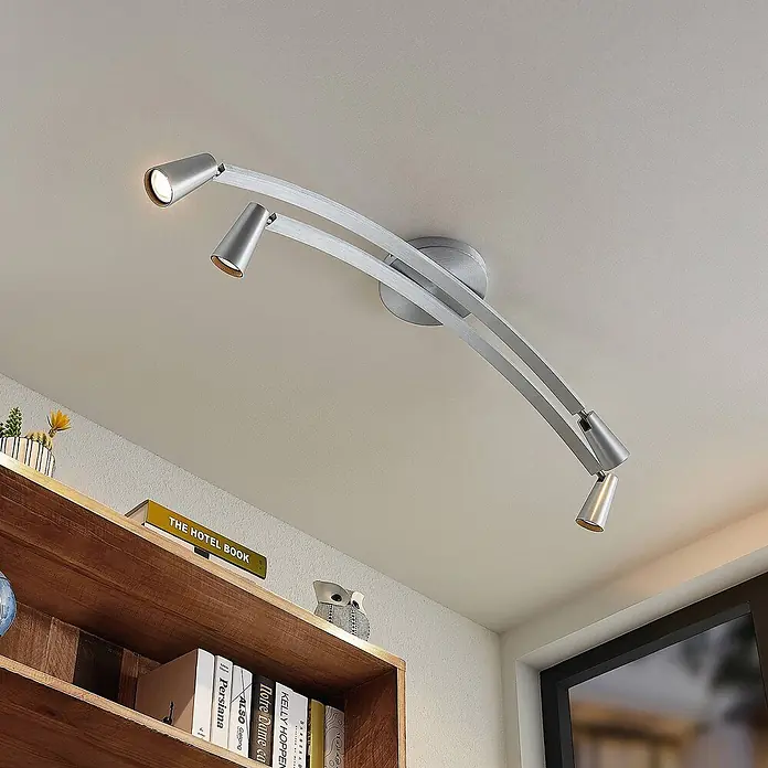 Lucande Deckenleuchte Velanoris - alu / grau / zink, alu / grau / zink, GU10 - Moderne silberfarbene Metalldeckenleuchte mit drei verstellbaren Strahlern beleuchtet einen Raum mit Holzbücherregal.
