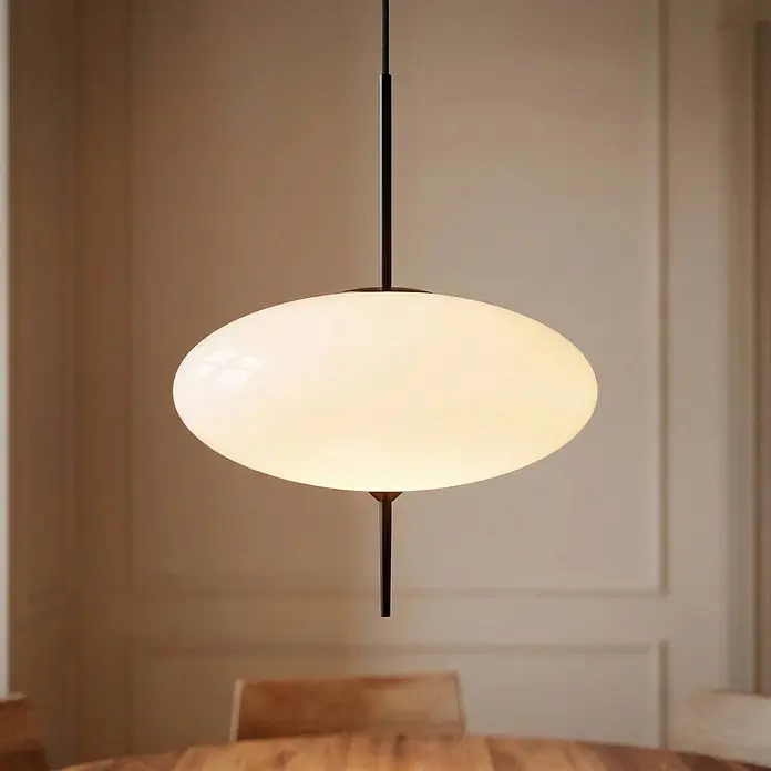 Lindby Pendelleuchte Hikari - weiß / opal, Schwarz, weiß, E14 - Ovale Pendelleuchte aus weißem Glas mit schwarzem Stab, beleuchtet über einem Holztisch.