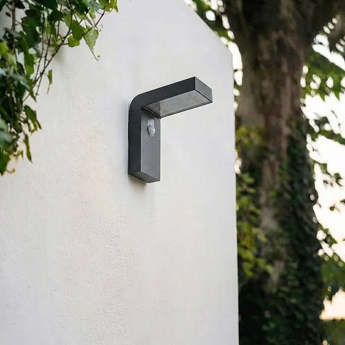Prios Außenwandleuchte Aurino - 20,5 x 9 x 20 cm, schwarz, IP44 - Dunkelgraue moderne rechteckige Außenwandleuchte mit integriertem Bewegungsmelder, an einer Fassade montiert.