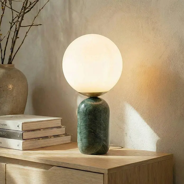 Lindby Tischleuchte Lennes - grün, weiß / opal, E27 - Beleuchtete Tischlampe mit weißem Glaskugel-Schirm und zylindrischem grünem Marmorfuß, auf heller Holzfläche neben Büchern.