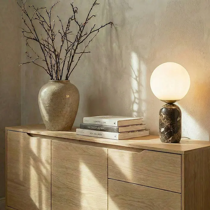 Lindby Tischleuchte Lennes - braun / rost, weiß / opal, E27 - Ein heller Holzschrank mit einer Vase voller Äste, Büchern und einer Kugellampe mit dunklem Marmorsockel.