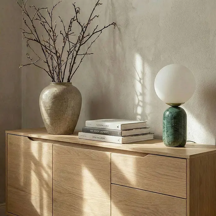 Lindby Tischleuchte Lennes - grün, weiß / opal, E27 - Helles Holzsideboard mit zwei Türen und zwei Schubladen, dekoriert mit einer Vase mit Ästen, Büchern und einer Marmorlampe.