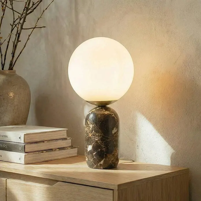 Lindby Tischleuchte Lennes - braun / rost, weiß / opal, E27 - Beleuchtete Tischlampe mit weißem Kugel-Diffusor und dunkelbraunem Marmorfuß auf einem Holzschrank.