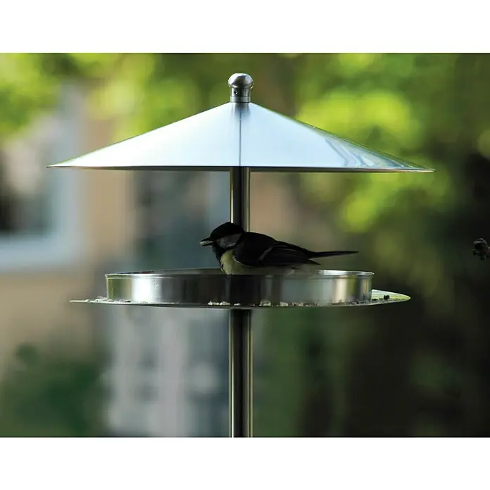 Dobar Vogelhaus Silberglanz - Durchmesser: 29 cm, Höhe: 125,5 cm, Silber, Edelstahl - Nahaufnahme eines stilvollen Vogelfutterhauses aus Edelstahl mit einem kleinen Vogel, der darauf sitzt und Körner pickt.