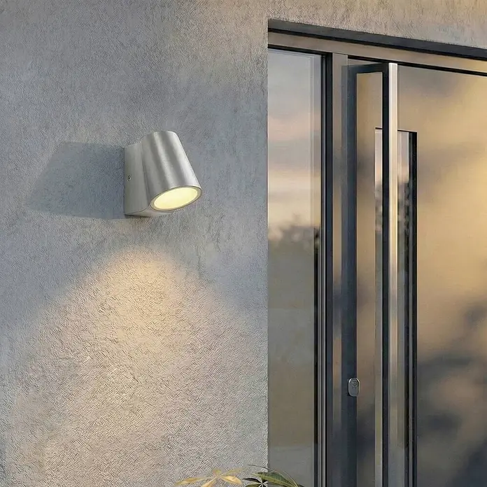 Lindby Außenwandleuchte Illuvia - alu / grau / zink, alu / grau / zink, IP44 - Gebürstete Metall-Außenwandleuchte mit Abwärtslicht, neben moderner Glastür montiert.