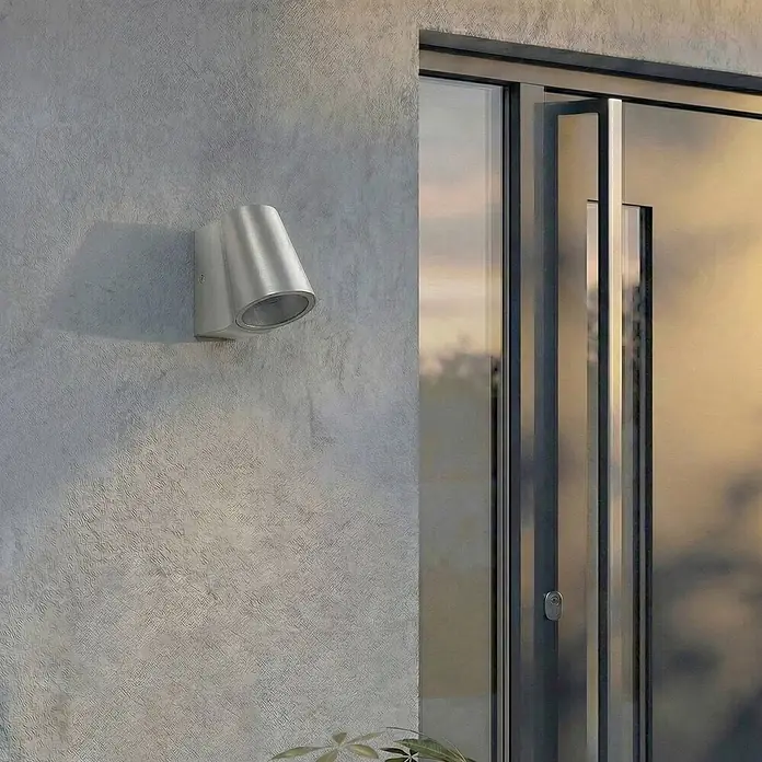 Lindby Außenwandleuchte Illuvia - alu / grau / zink, alu / grau / zink, IP44 - Silberne metallene Außenwandleuchte, konisch geformt, an einer strukturierten Wand montiert.
