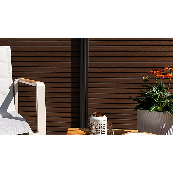 GartenLand Steckzaun-Element Shadowline - B x H: 180 x 180 cm, Ipé, Verbundwerkstoff - Weißer Outdoor-Stuhl mit Holzarmlehnen und Topf-Orangenblüten auf einem Holztisch, vor einer braunen Lamellenwand.