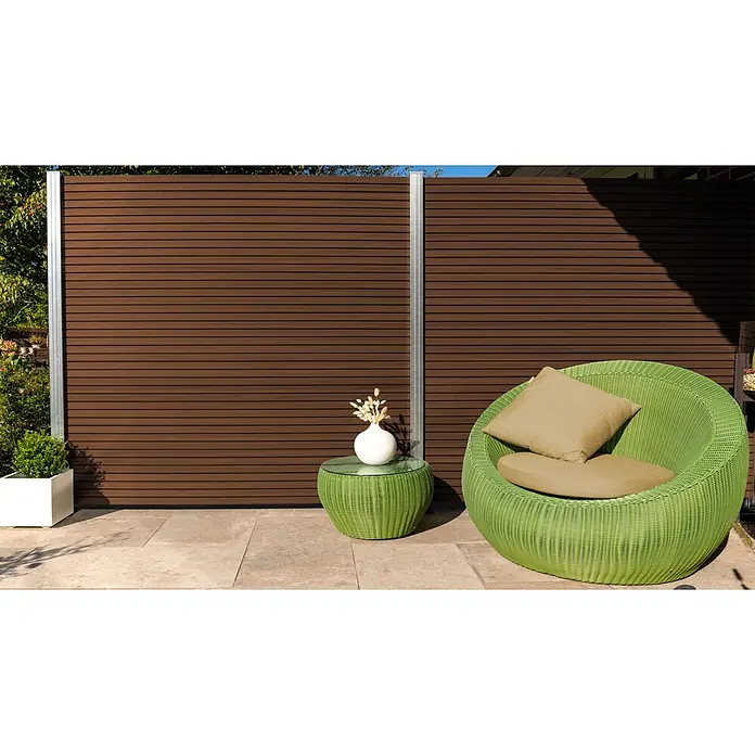 GartenLand Steckzaun-Element Shadowline - B x H: 180 x 180 cm, Ipé, Verbundwerkstoff - Ein leuchtend grüner Korb-Gartensessel mit beigen Kissen und passendem Beistelltisch mit Glasplatte und weißer Vase auf einer Terrasse.