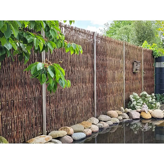 GartenLand Sichtschutzelement Sylt - B x H: 180 x 180 cm, Holz, Btaun - Geflochtener Weidenzaun, dunkelbraun, als natürlicher Sichtschutz in einem Garten neben einem Teich.