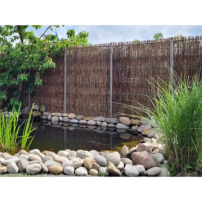 GartenLand Sichtschutzelement Sylt - B x H: 120 x 180 cm, Holz, Braun - Ein Gartenbrunnen mit dunklem Wasser, umgeben von Ziersteinen, vor einem hohen, geflochtenen braunen Weidenzaun.