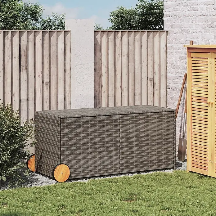 Furnicato Garten-Aufbewahrungsbox - Grau, Naturmaterialien - Dunkelgraue Rattan-Gartenbox mit Holzrädern, auf Kies neben Gras im Garten platziert.