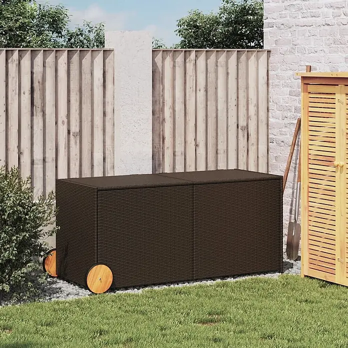 Furnicato Garten-Aufbewahrungsbox - Braun, Naturmaterialien - Dunkelbraune Rattan-Gartenbox mit Holzrädern, auf Kies im Garten vor einem Holzzaun.