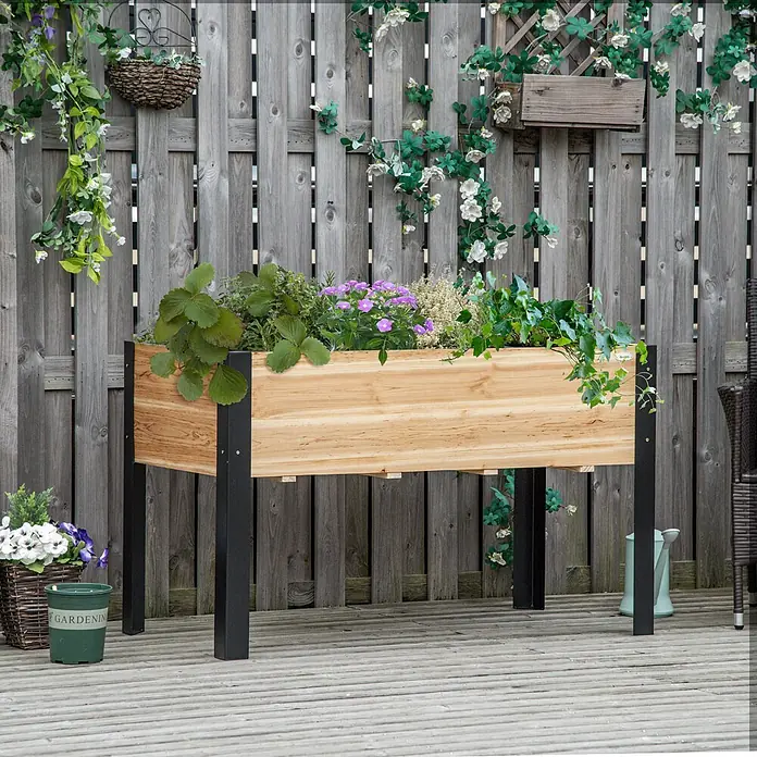 Outsunny Kräuterhochbeet - Material: Holz - Ein helles Holzhochbeet mit schwarzen Beinen ist mit bunten Pflanzen und Kräutern gefüllt, auf einer Terrasse vor einem Holzzaun stehend.
