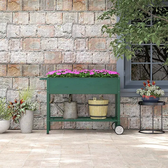 Outsunny Kräuterhochbeet - Material: Metall - Grünes Hochbeet mit Rollen, voller rosa Blumen, mit Gießkanne und Eimer auf der Ablage auf einer Terrasse.