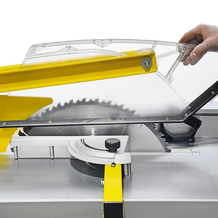 BAMATO Tischkreissäge BCS-500PRO 400V 4200W 500mm Sägeblatt -  - Transparenter Sägeblattschutz mit gelbem Arm über einer Tischkreissäge, von einer Hand eingestellt.