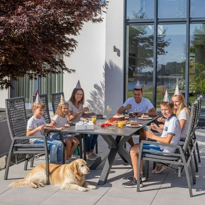 Bene Living Gartentisch-Set Lucena mit Tisch Malaga - Gesamtumfang: 7 -tlg., Aluminium pulverbeschichtet, Textilene, Rope-Geflecht und Tischplatte aus gesintertem Stein (Keramik), Rückenlehne verstellbar - Graues Outdoor-Essgruppe mit einer Familie, die auf der Terrasse einen Geburtstag feiert.