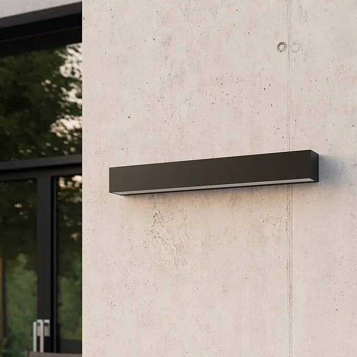 Lucande Außenwandleuchte Lengo - schwarz, schwarz, IP65 - Dunkle rechteckige Wandleuchte an Betonwand, links Fenster und Grün zu sehen.