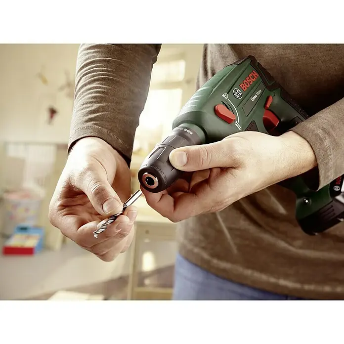 Bosch Power for All 18V Martillo perforador de batería Uneo MAXX - 18 V, 1 batería, 0,6 J - Primer plano de una persona que inserta una broca en un taladro inalámbrico verde Bosch Uneo Maxx.