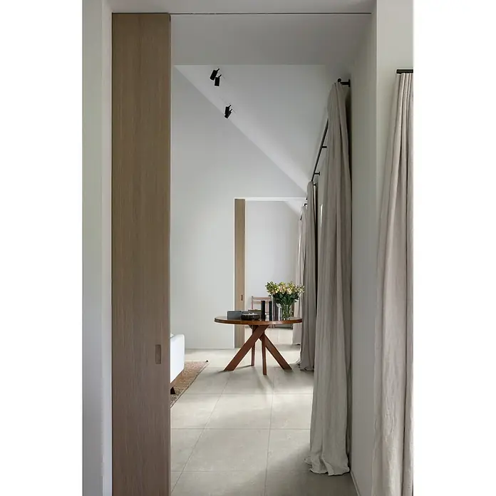 Feinsteinzeugfliese Cortina - 60 x 60 cm, Bianco, Matt - Moderner Flur mit hellgrauem Fliesenboden, einem runden Holztisch und natürlichen Leinenvorhängen.