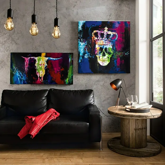 Handgemaltes Bild Handgemalt - Colourful Bull I, B x H: 120 x 60 cm - Das Bild zeigt eine moderne schwarze Couch mit Kunstwerken und einer Lampe auf einem Holztisch. Rote Jacke liegt auf der Couch.