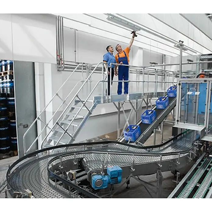 Munk Außentreppe Treppen-Modul 1460mm Plattformoberkante Aluminium geriffelt 7 Stufen - 80 cm, Anzahl Steigungen: 7 Stk. - Automatisiertes Förderbandsystem mit Kurvenabschnitten, das blaue Kisten in einer Industrieanlage transportiert, beobachtet von Arbeitern auf einer Metallplattform.