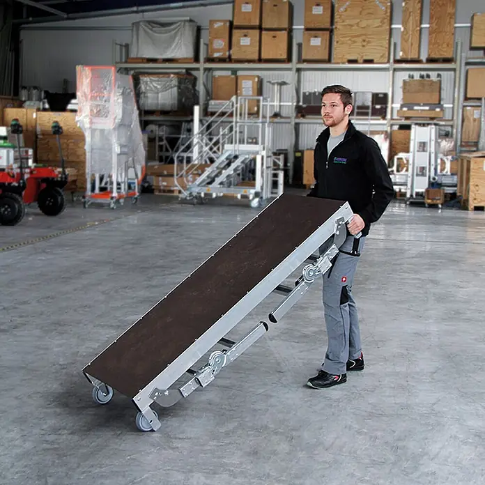 Munk Arbeitsplattform ML Maschinenpodest höhenverstellbar - Anzahl Tritte: 3 Stk., Arbeitshöhe: 2.730 m, Aluminium - Mann bewegt ein tragbares Förderband mit dunklem Gurt, Aluminiumrahmen und Rollen auf Lagerboden.