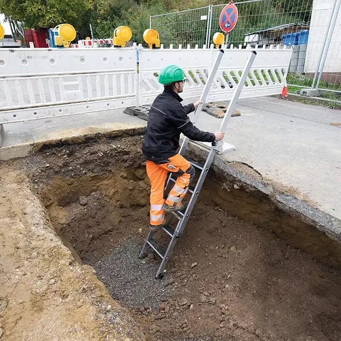 Munk Anlegeleiter Stufen-Baugrubenleiter 2,25m mit 4 Stufen mit Handlauf - Anzahl Tritte: 4 Stk., Arbeitshöhe: 3.050 m, Aluminium - Silberne Zugangsleiter, die ein Arbeiter benutzt, um aus einem Graben auf einer Baustelle zu steigen.