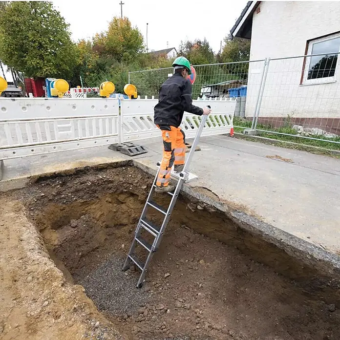 Munk Anlegeleiter Stufen-Baugrubenleiter 2,25m mit 4 Stufen mit Handlauf - Anzahl Tritte: 4 Stk., Arbeitshöhe: 3.050 m, Aluminium - Metall-Zugangsleiter mit Plattform, von einem Arbeiter zum Abstieg in eine Baugrube genutzt.