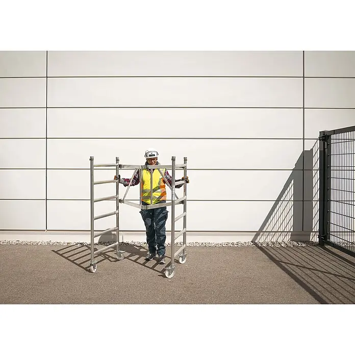 Werner Rollgerüst Klappgerüst Tower 3T nach DIN Norm EN 1004-1 AH 7,55m - Arbeitshöhe: 7.550 m, Belastbarkeit Plattform: 216 kg - Eine Person in Arbeitskleidung schiebt ein silberfarbenes Aluminium-Rollgerüst.