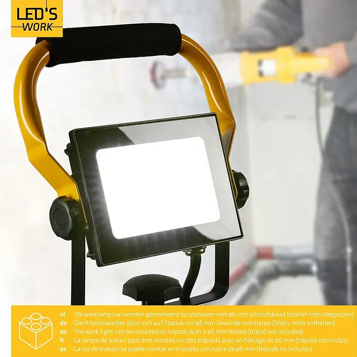 LED's work LED-Arbeitsleuchte - L x B x H: 18 x 18 x 24 cm, 2.700 lm, Lichtfarbe: Neutralweiß, Netzbetrieben, IP65 - Eine helle LED-Arbeitsleuchte mit gelbem Rahmen und schwarzem Griff, die einen Arbeitsbereich beleuchtet.